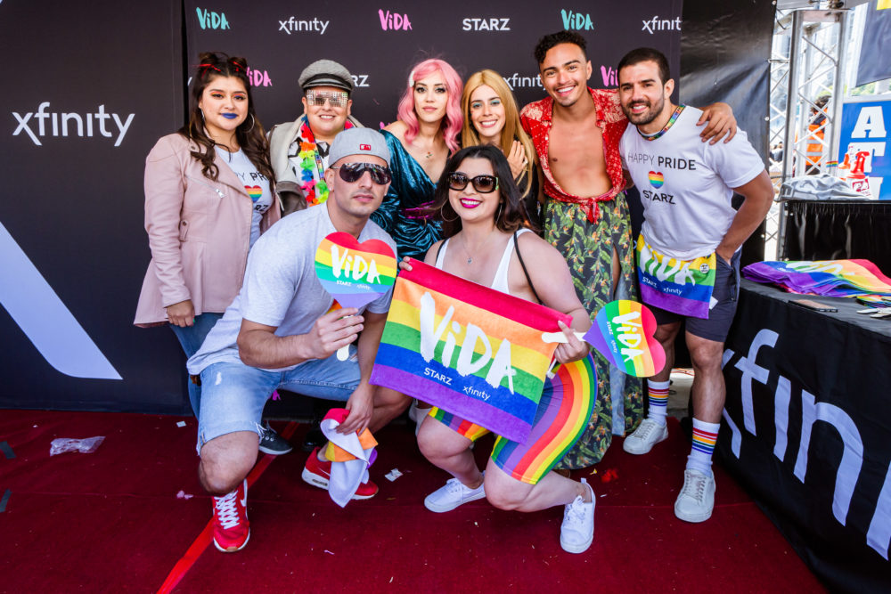 Group of people posing for picture together holding pride flag.