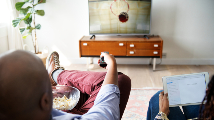 Two people sit on a couch and use a remote to watch TV.